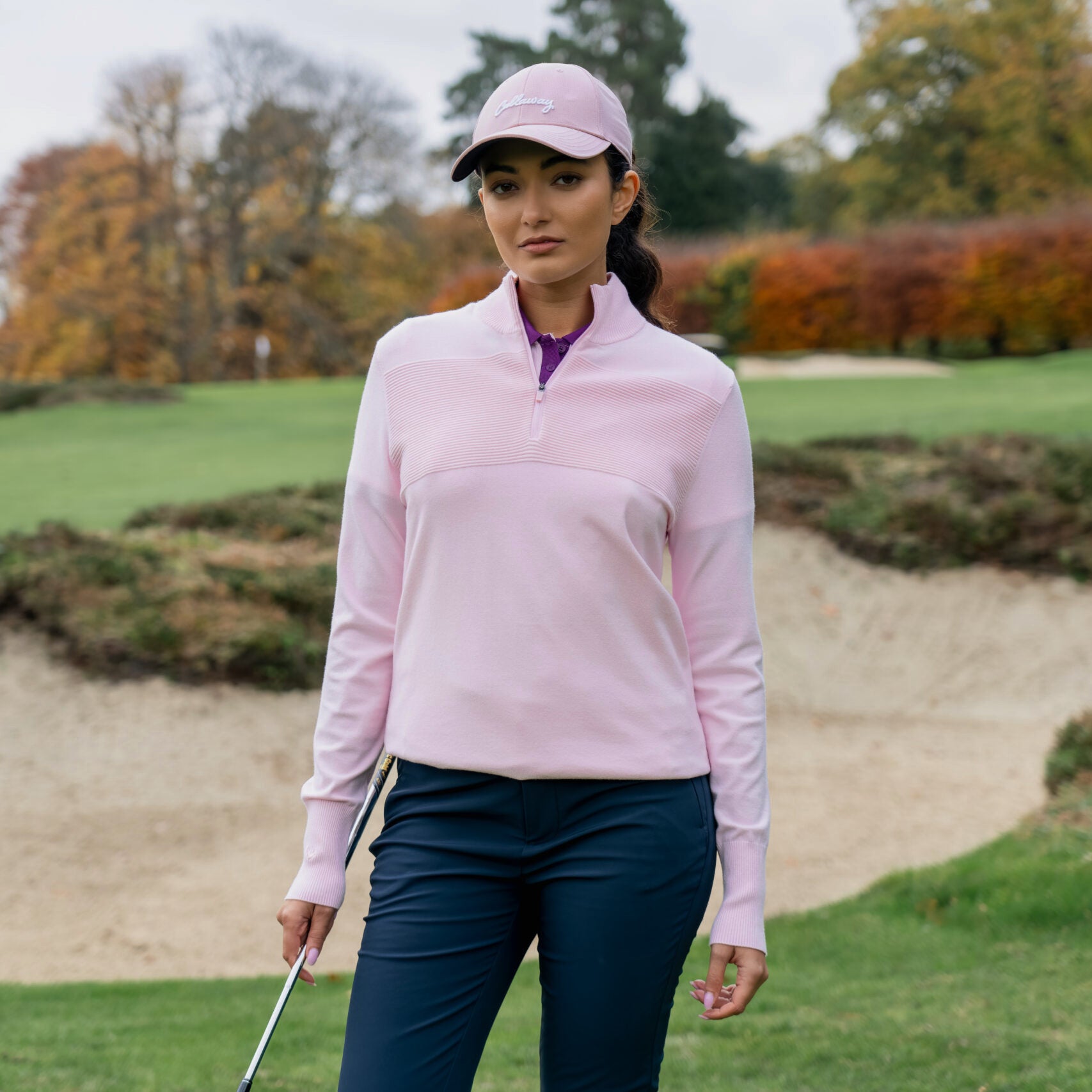 Vrouwelijke golfer draagt de Callaway Soft Stretch Zip-Neck Sweater in Cherry Blossom op de golfbaan