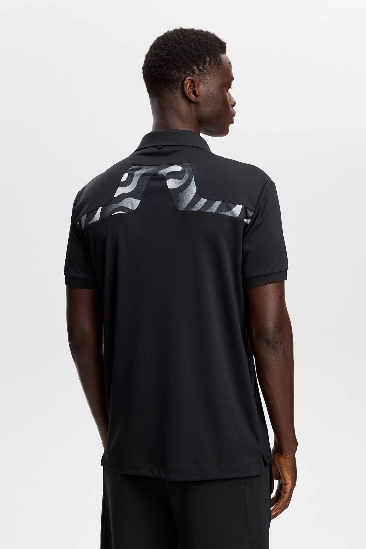 J.Lindeberg KV Print Polo Zwart – lifestyle shot op de baan met UPF 40+ zonbescherming